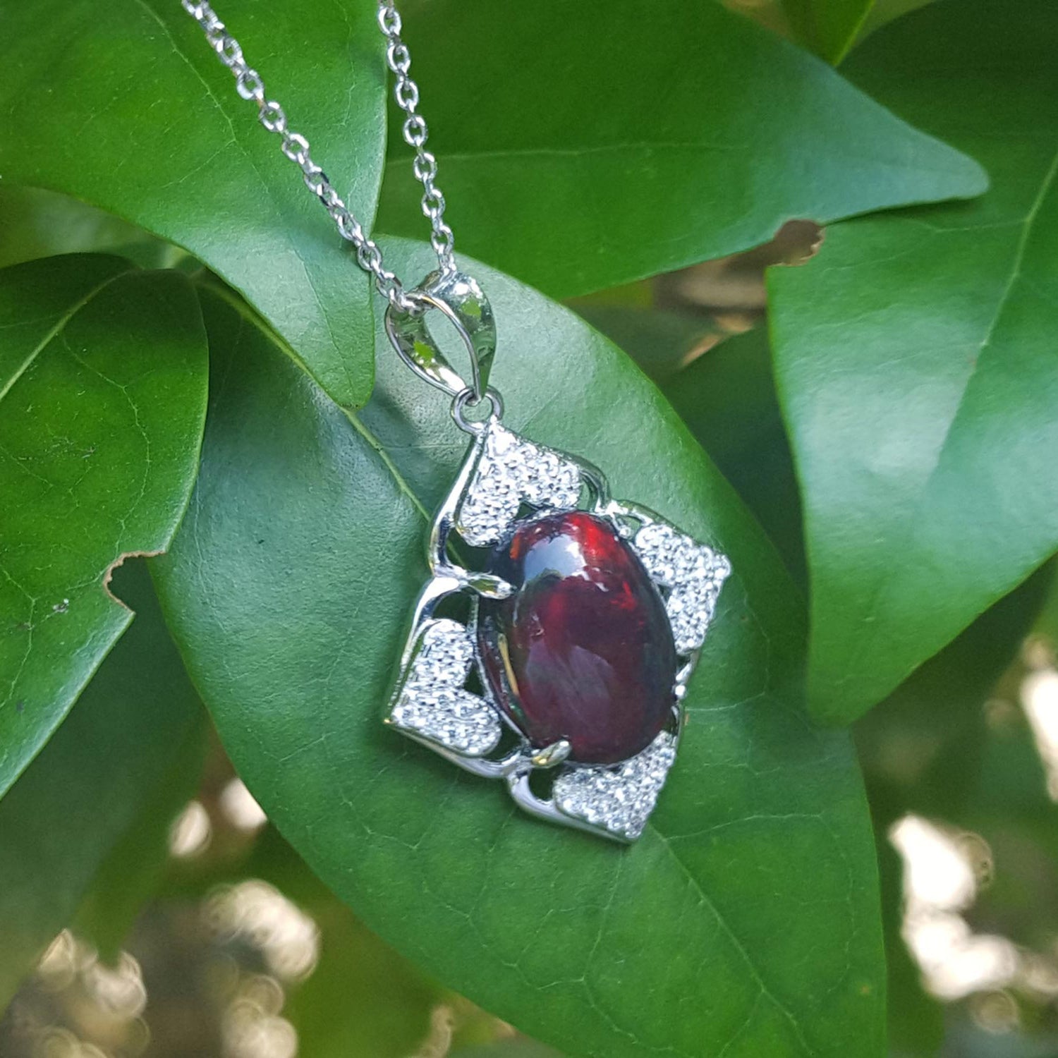 Silver pendant with a black Welo opal on a green leaf background.