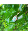 Opal pendant necklace on a green leaf with a blurred green foliage background