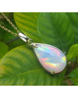 Opal pendant necklace on a gold chain against a green leaves background.