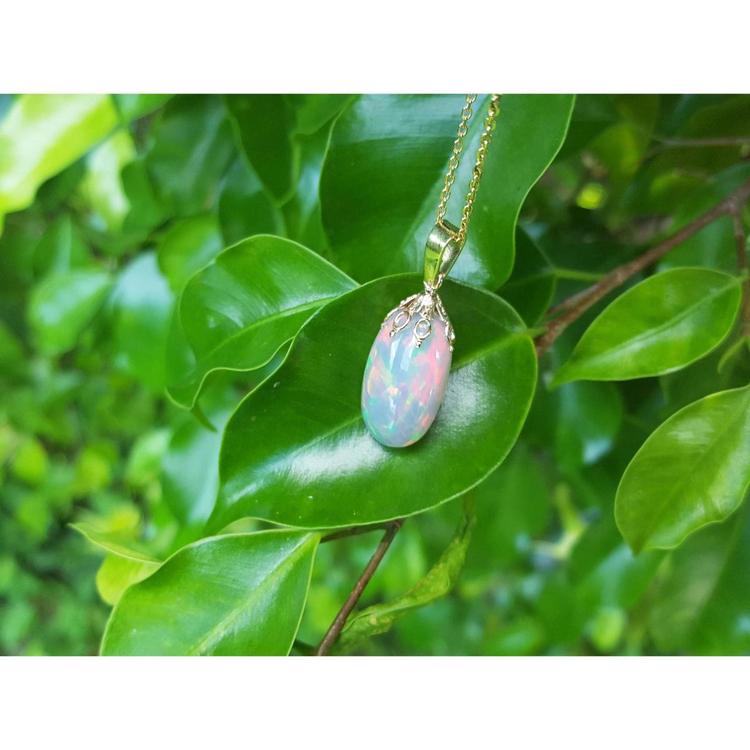 Ethiopian Welo opal pendant with red fire, set in 14k yellow gold, hanging on a green leaf.