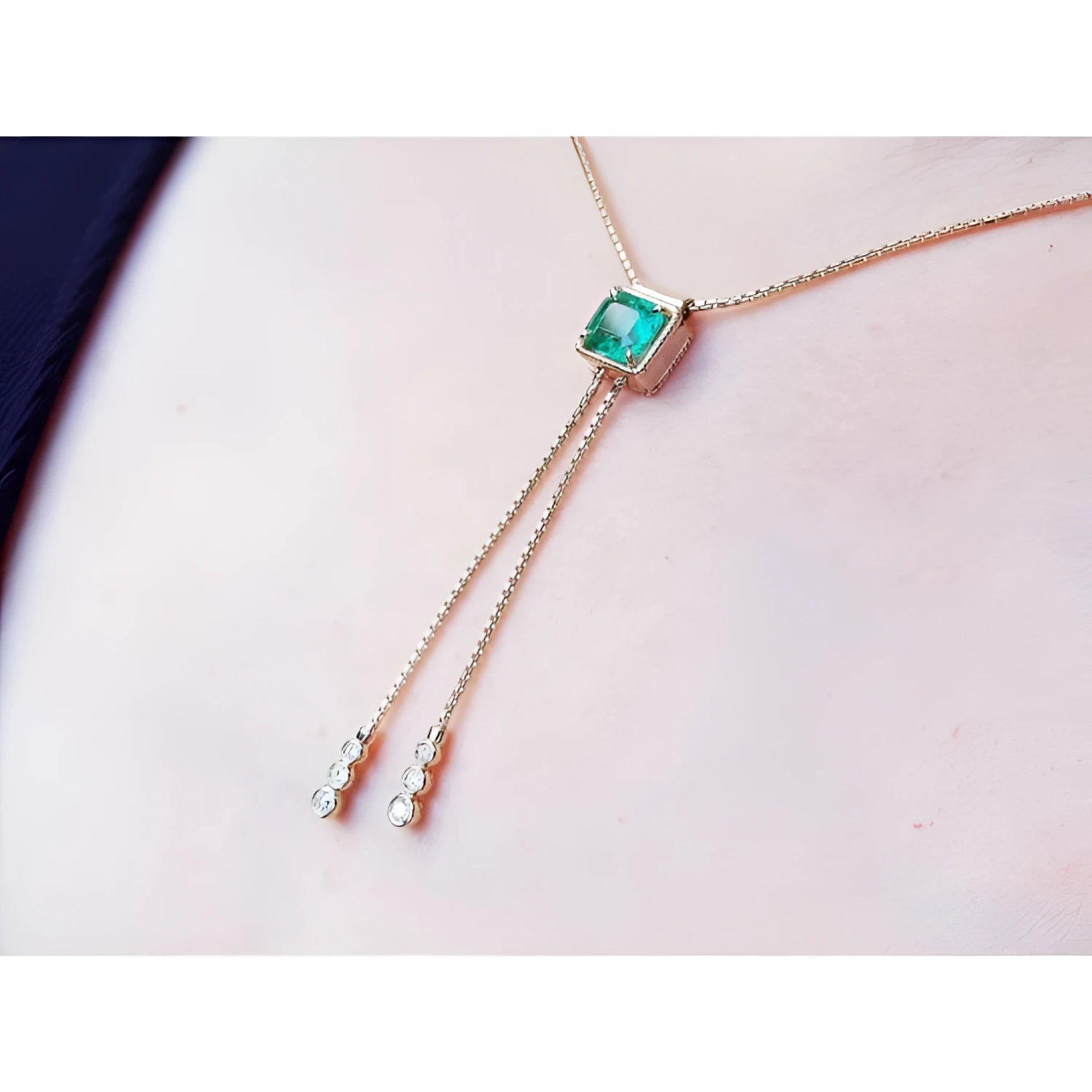 14K gold lariat necklace with a square emerald pendant and two dangling diamond accents on a box chain.