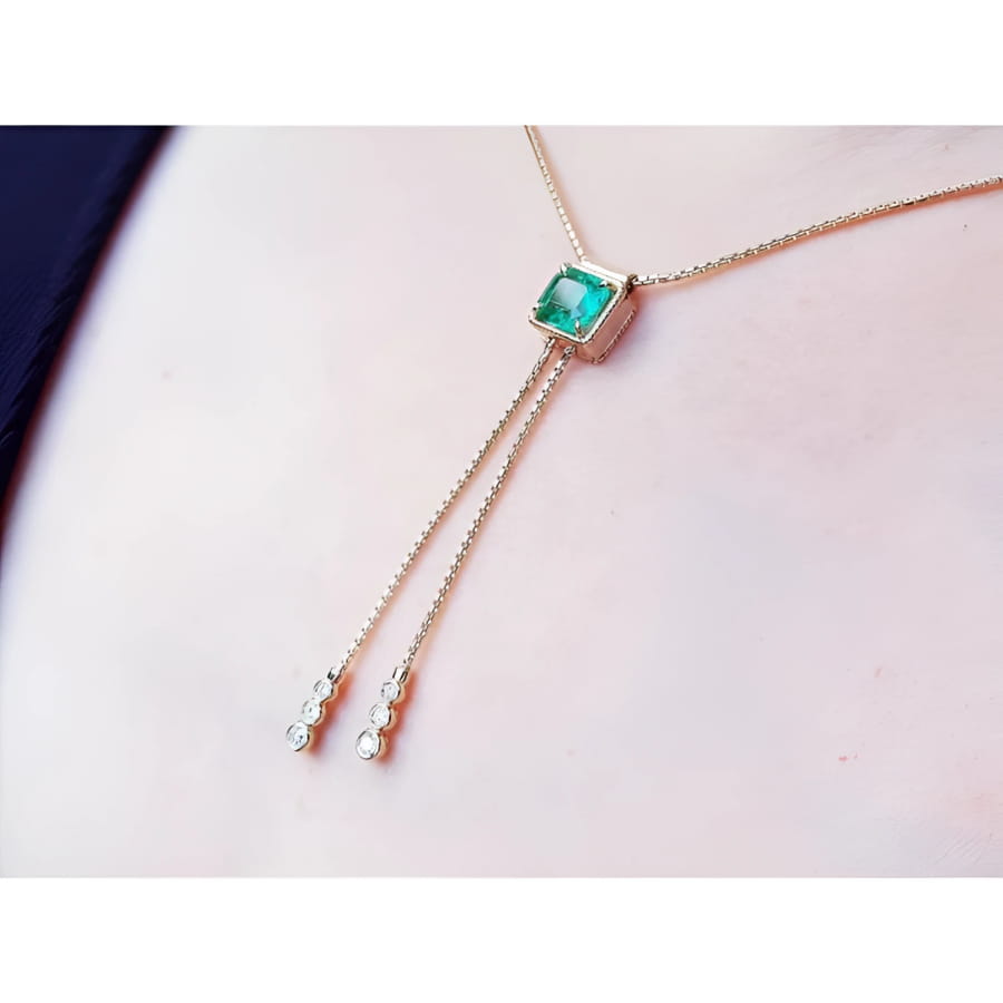 14K gold lariat necklace with a square emerald pendant and two dangling diamond accents on a box chain.
