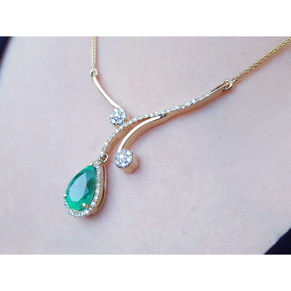 left side of a yellow gold necklace with a Colombian emerald teardrop pendant on a person&#39;s neck
