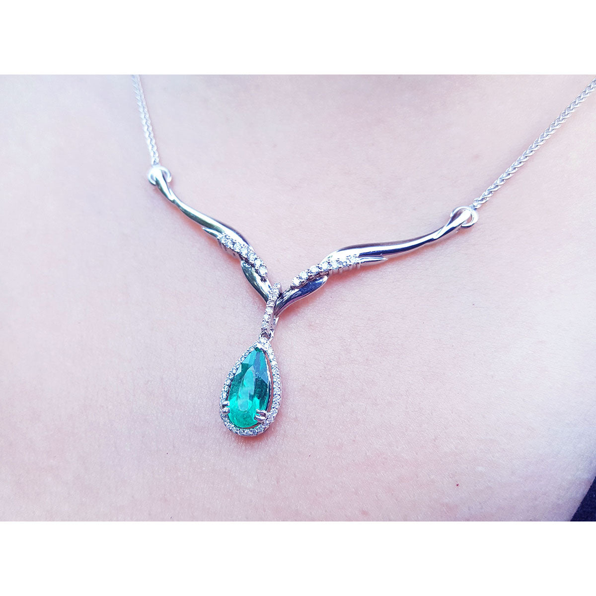 A left side view of a white gold 14k necklace with tear drop emerald in a halo natural diamond