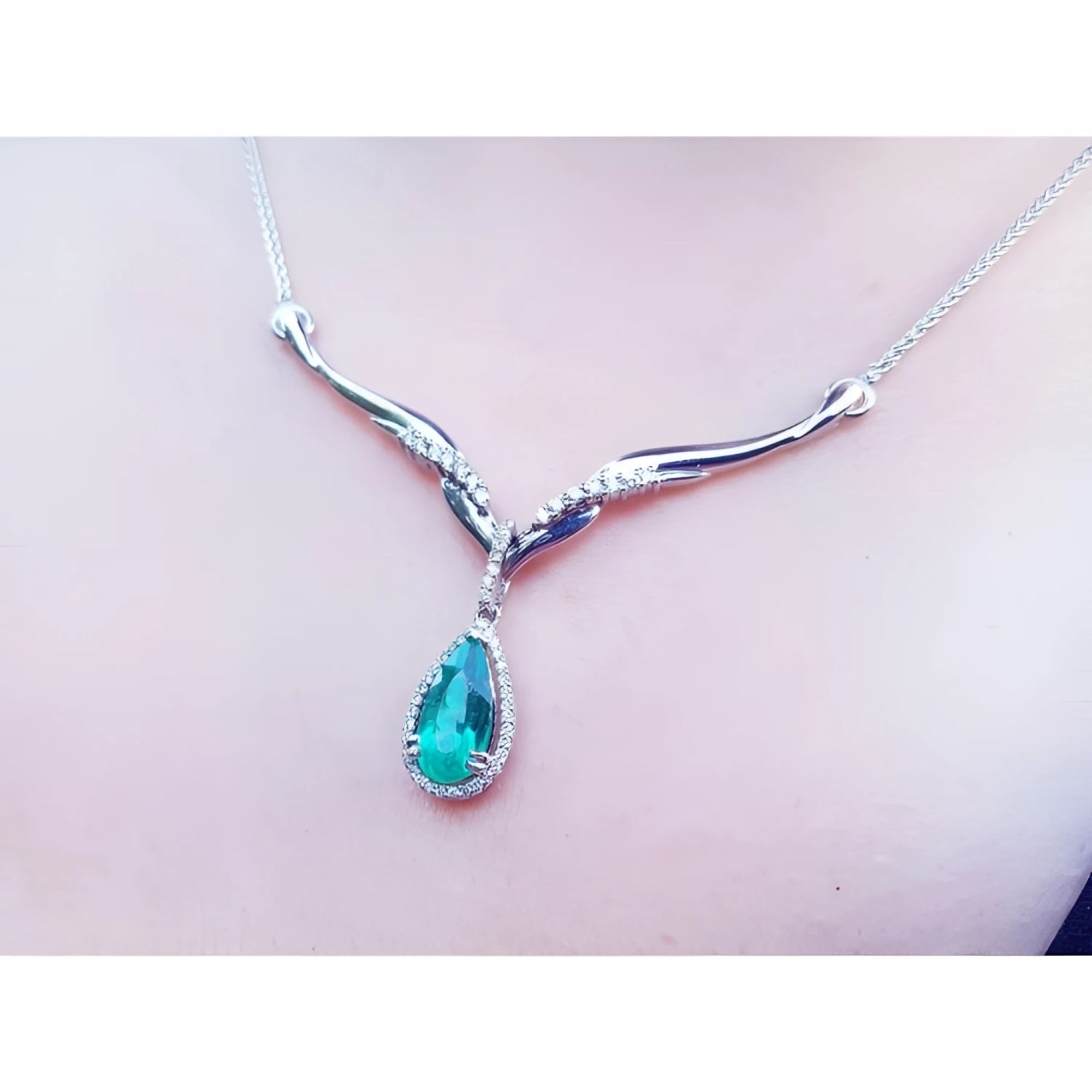 14K white gold necklace with a pear-cut emerald pendant surrounded by diamonds and an entwined chevron design.
