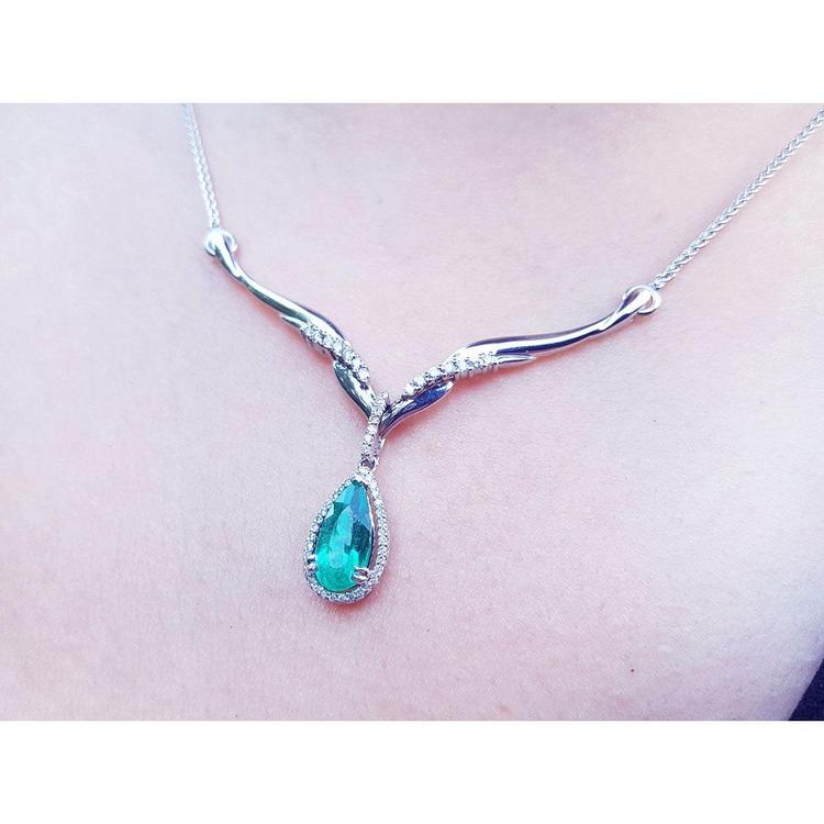 14K white gold necklace with a pear-cut emerald pendant surrounded by diamonds and an entwined chevron design.