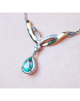 A left side jewelry necklace with a dangling teardrop emerald gemstone solitaire pendant on woman's collar