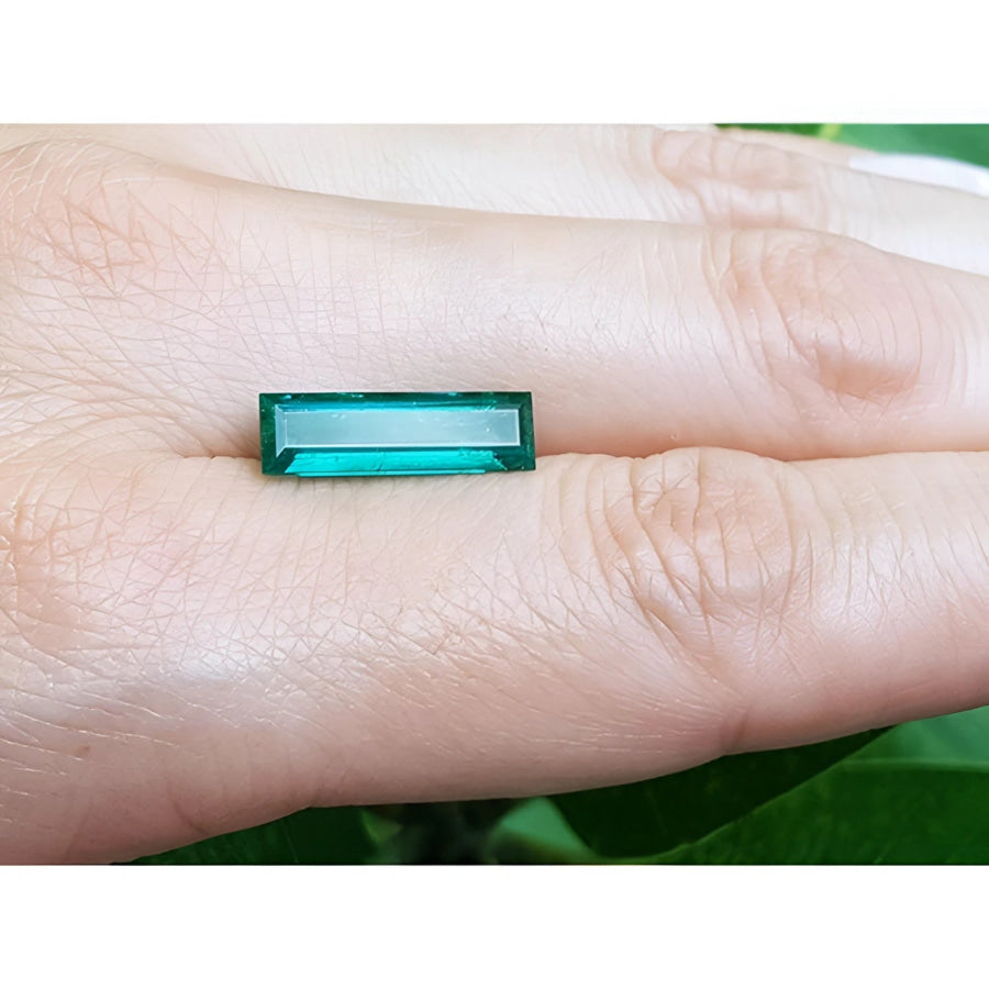 3.13 carat baguette cut Colombian emerald, sparkling bluish-green, held on a finger.