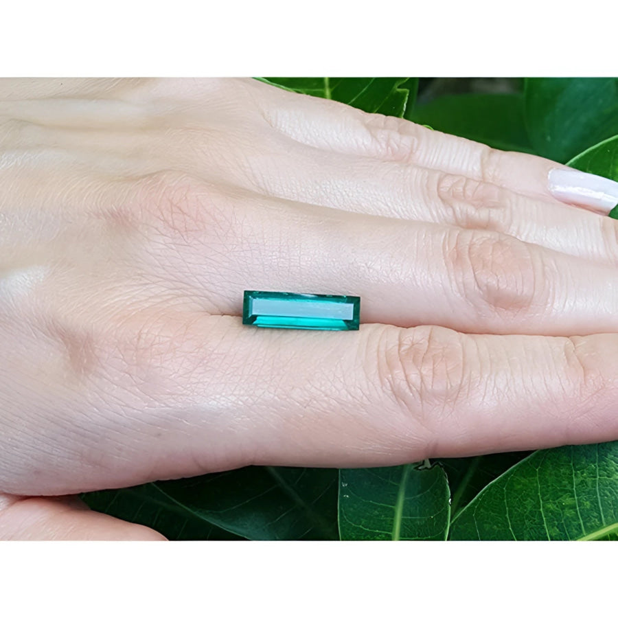 3.13 carat baguette cut Colombian emerald, eye clean, sparkling bluish-green, held on a hand.