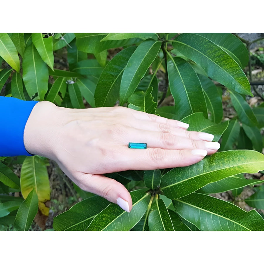 3.13 carat baguette cut Colombian emerald, eye-clean, sparkling bluish-green, on a hand against green leaves.