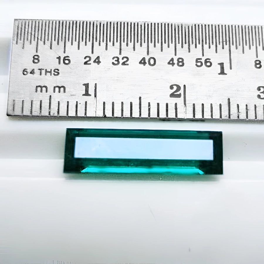 Baguette cut Colombian emerald, sparkling bluish-green, shown with a ruler for scale.