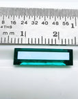 Baguette cut Colombian emerald, sparkling bluish-green, shown with a ruler for scale.