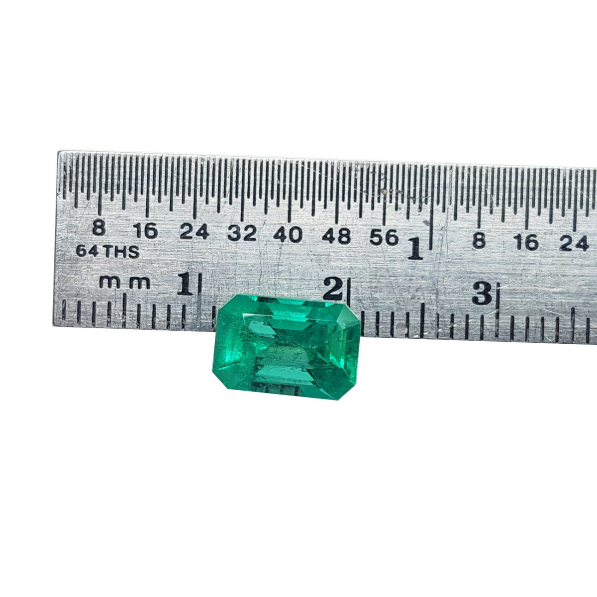 A loose natural Colombian emerald placed next to a ruler to show size measurement.