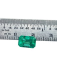 A loose natural Colombian emerald placed next to a ruler to show size measurement.
