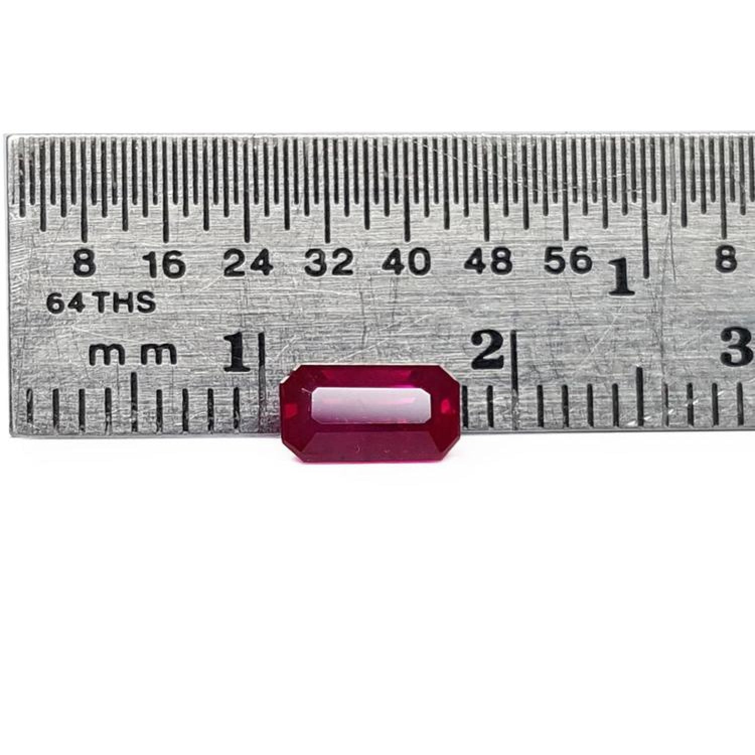 0.94 carat natural Burma ruby, emerald cut, vibrant red, displayed on a ruler.