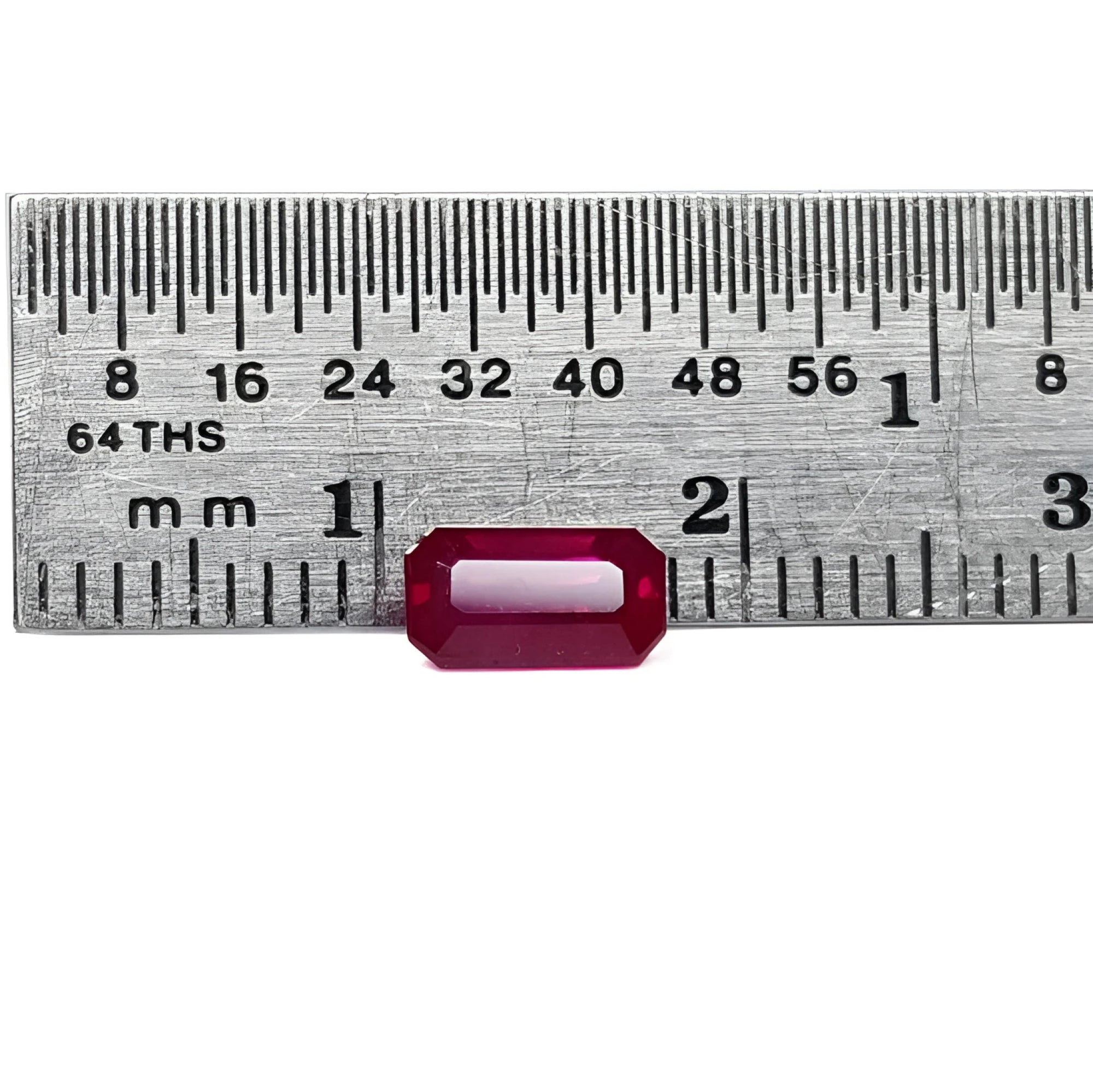 0.94 carat natural Burma ruby, emerald cut, vibrant red, displayed on a ruler.
