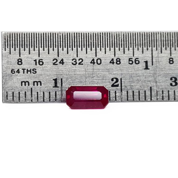 0.94 carat natural Burma ruby, emerald cut, vibrant red, displayed on a ruler.