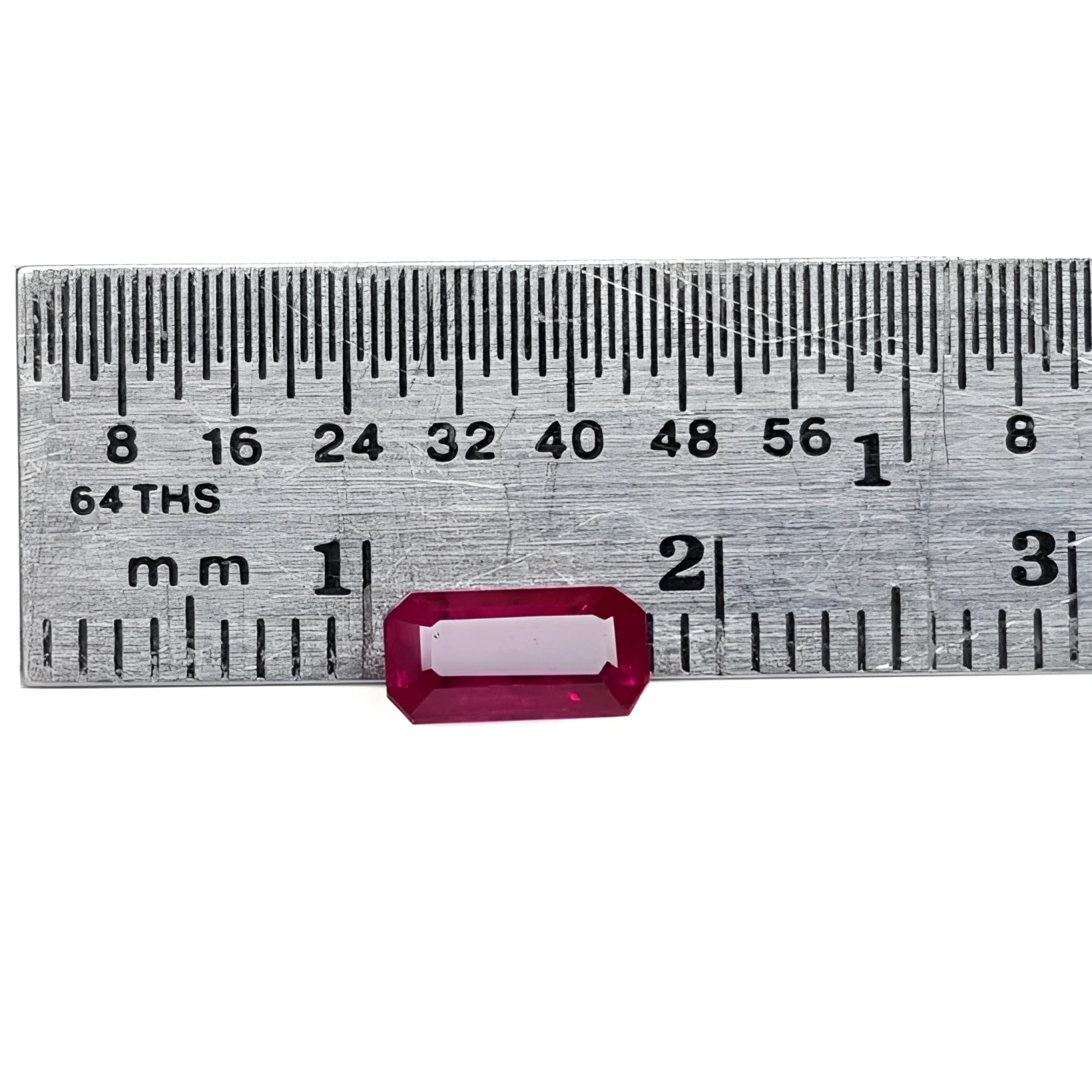 Sparkling 0.97 carat medium deep rich red emerald cut natural Burma loose ruby next to a ruler.
