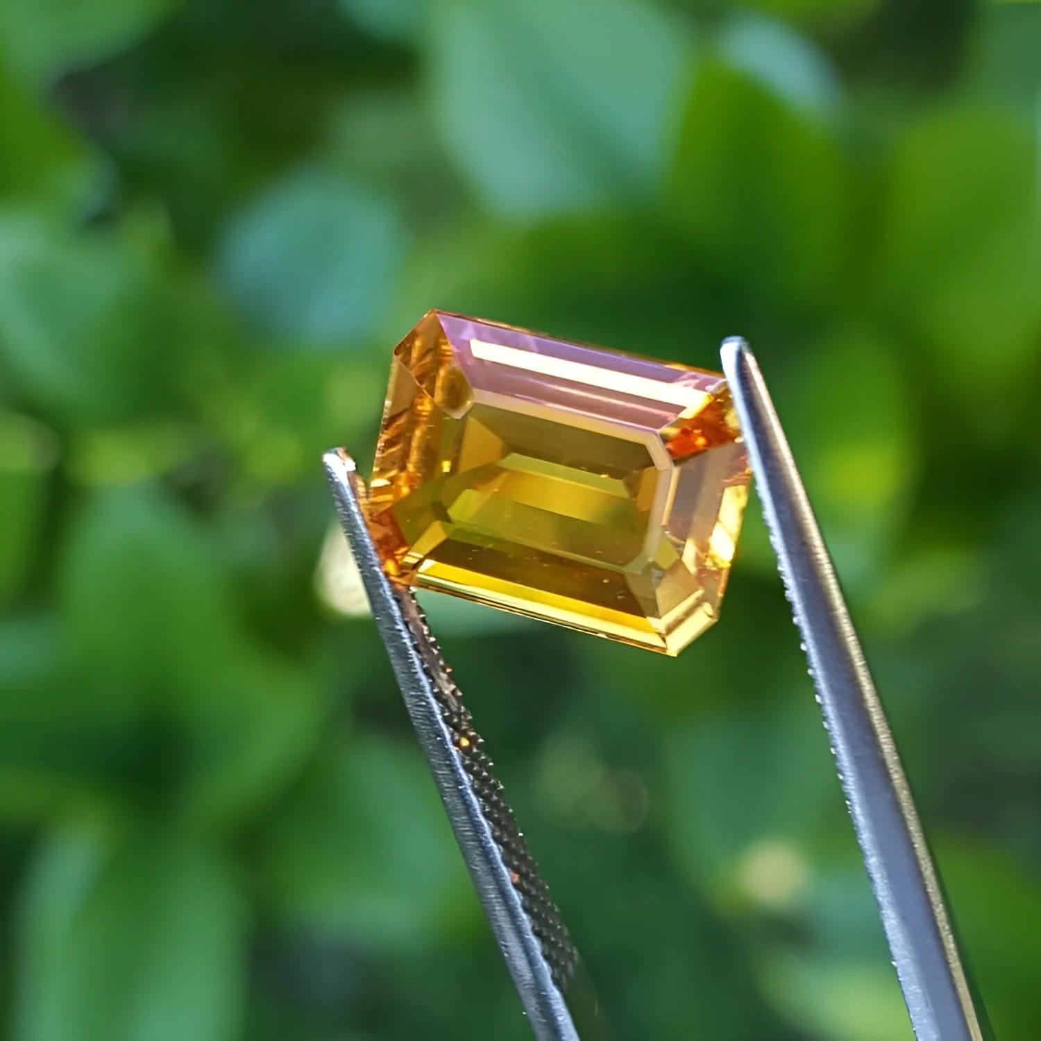 4.05 ct. vibrant intense yellow sapphire gemstone, emerald-cut, held by tweezers against a green background.