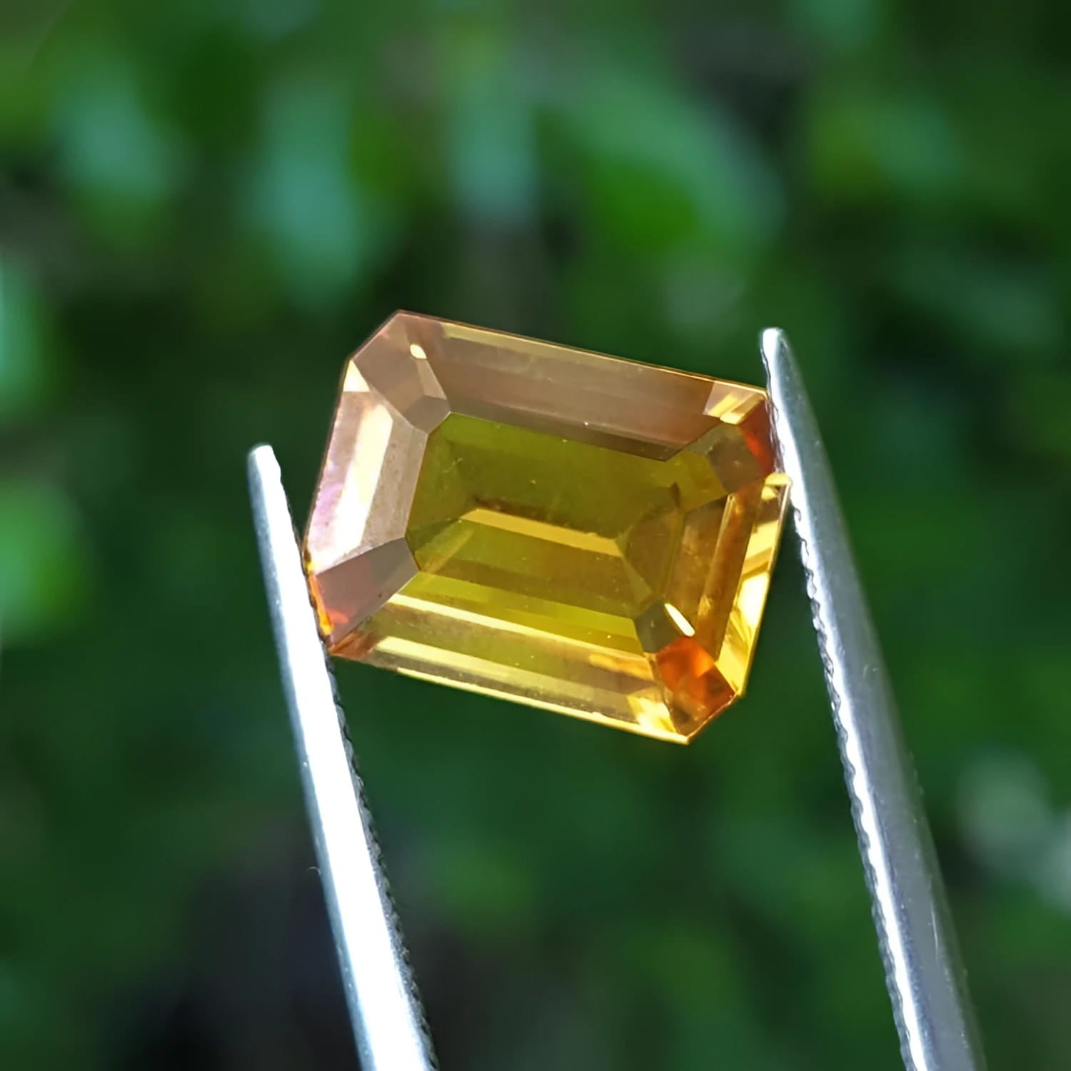 4.05 ct natural intense yellow emerald-cut sapphire gemstone held by tweezers.