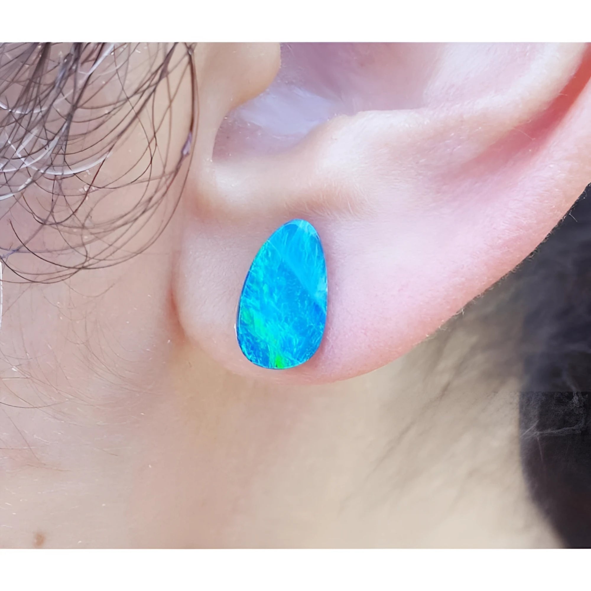 Pear-shaped deep blue Australian doublet opal earring on an earlobe.