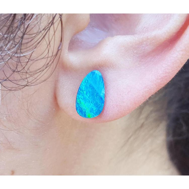 A closer view of an ear wearing a blue opal stud earring.