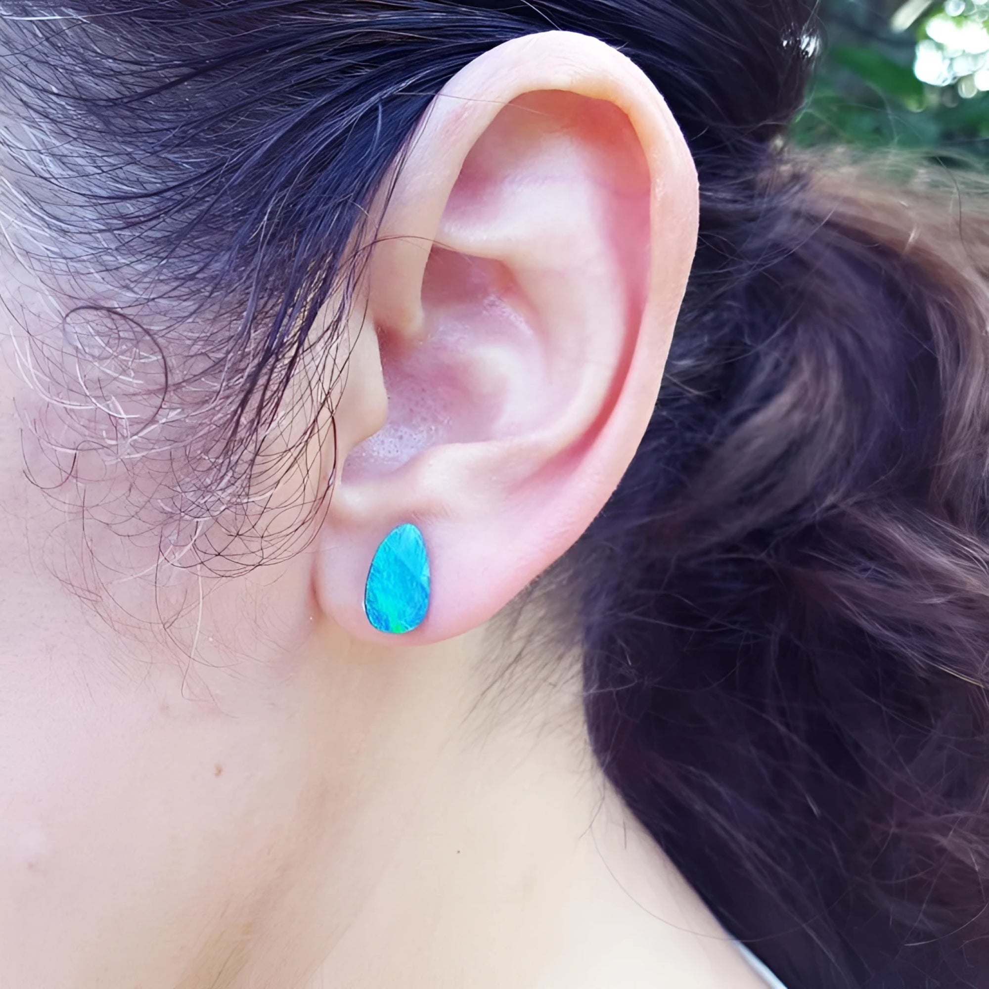 Pear-shaped deep blue Australian doublet opal earring on an ear.