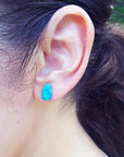 Close-up of an ear wearing a blue opal earring with blurred background