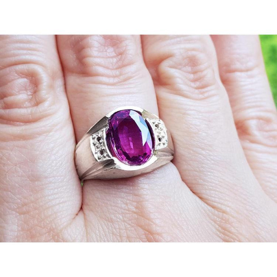 Oval-cut natural pink sapphire ring with sparkling medium pink stone and white accents on a hand.