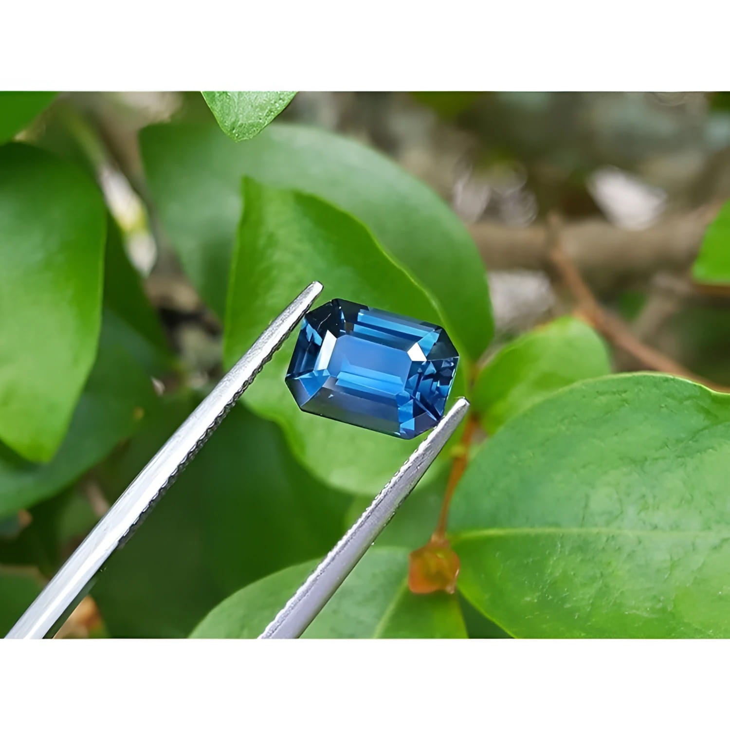 GIA-certified 3.53 ct. natural greenish-blue emerald cut sapphire held by tweezers.