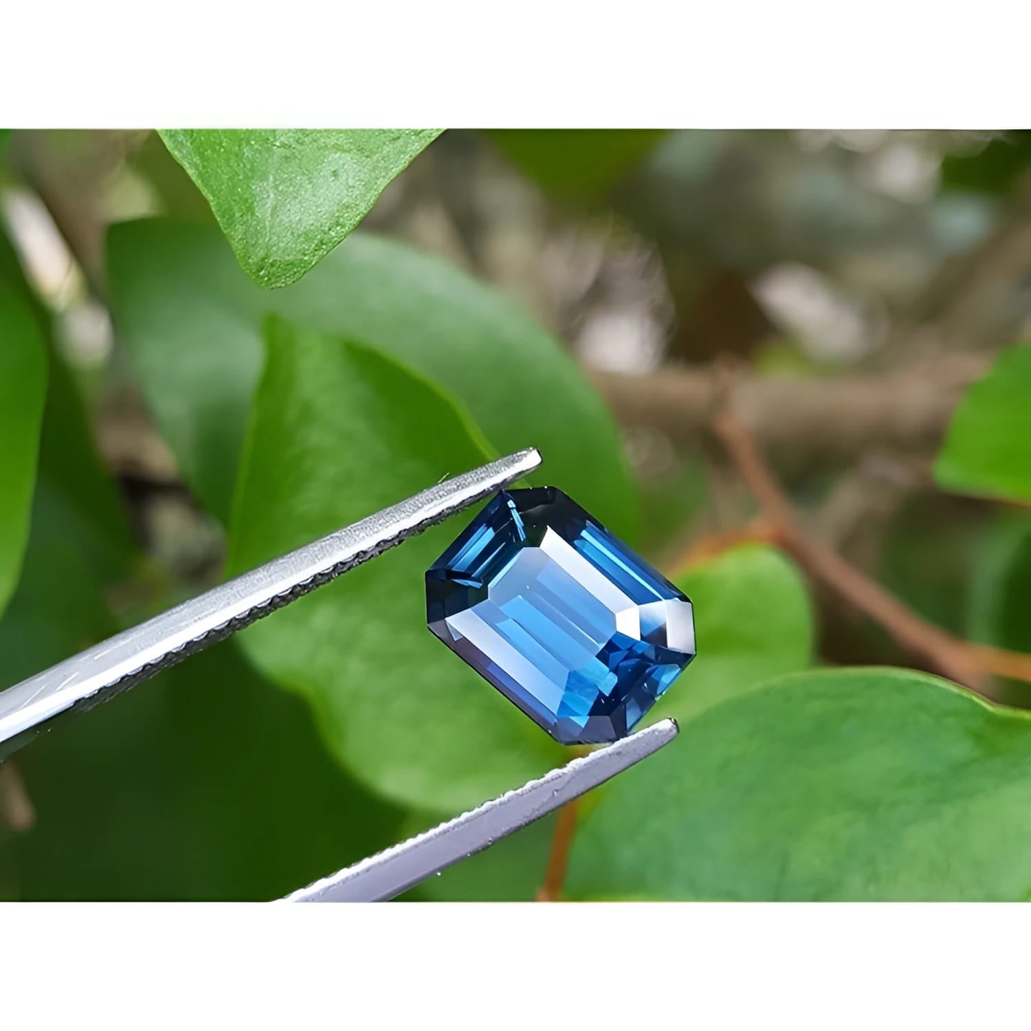 GIA-certified 3.53 ct. rectangular emerald cut natural greenish-blue sapphire held by tweezers.