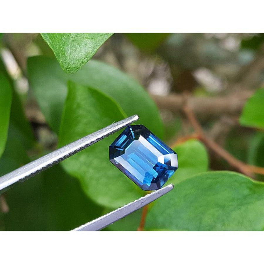 GIA-certified 3.53 ct. rectangular emerald cut natural greenish-blue sapphire held by tweezers.