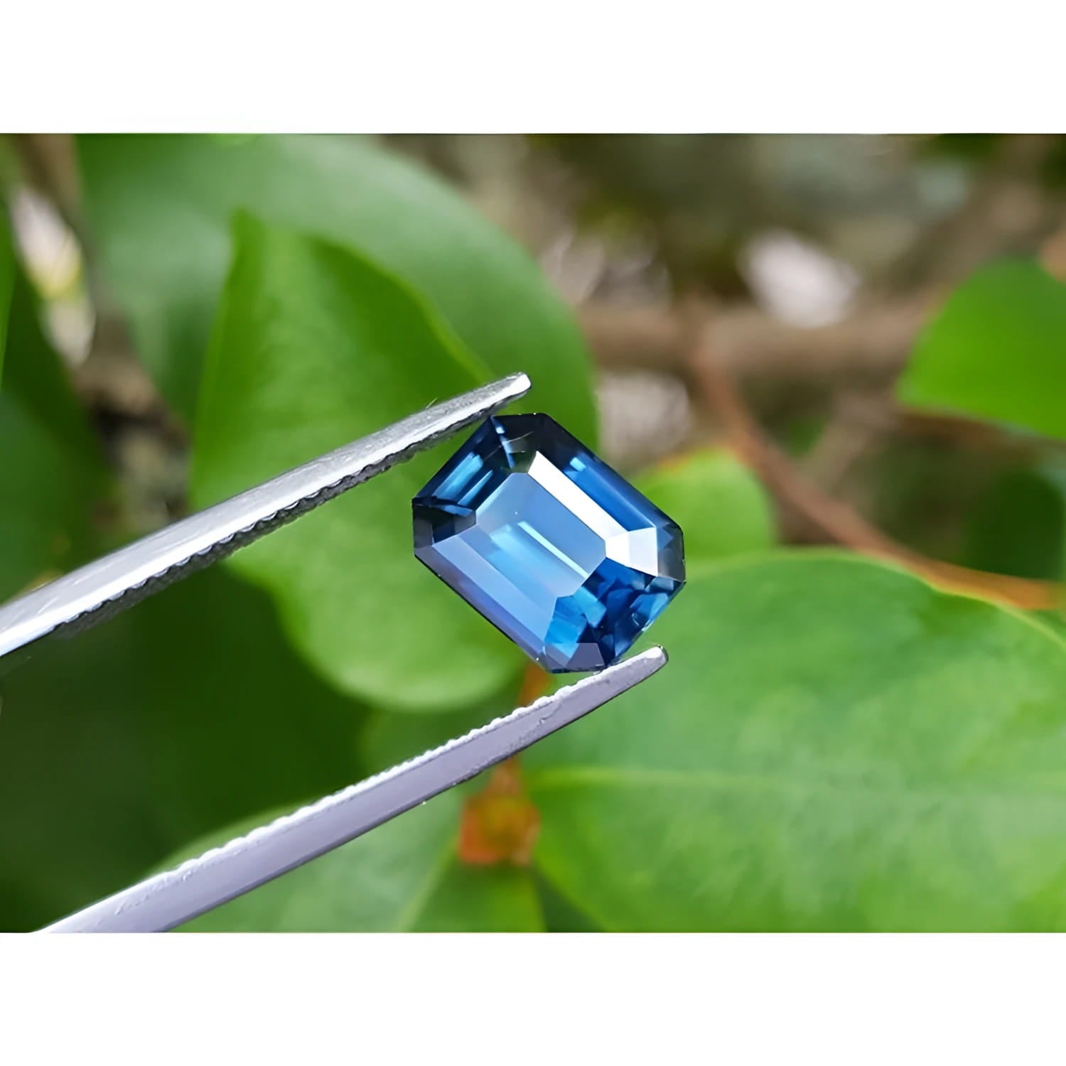 3.53 ct GIA certified natural greenish-blue sapphire, rectangular emerald cut, held by tweezers.