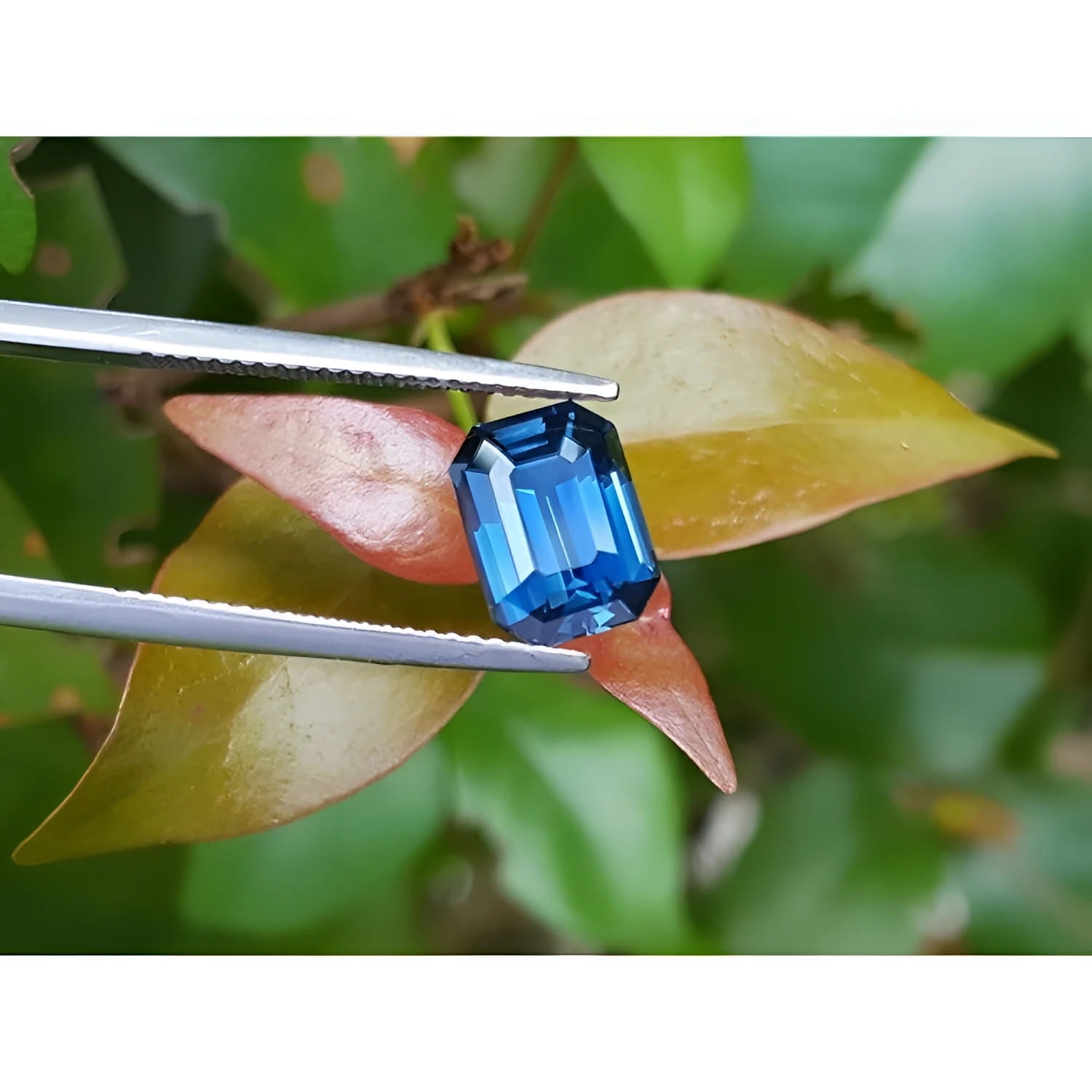 GIA-certified 3.53 ct. natural greenish-blue sapphire, rectangular emerald cut, held by tweezers.