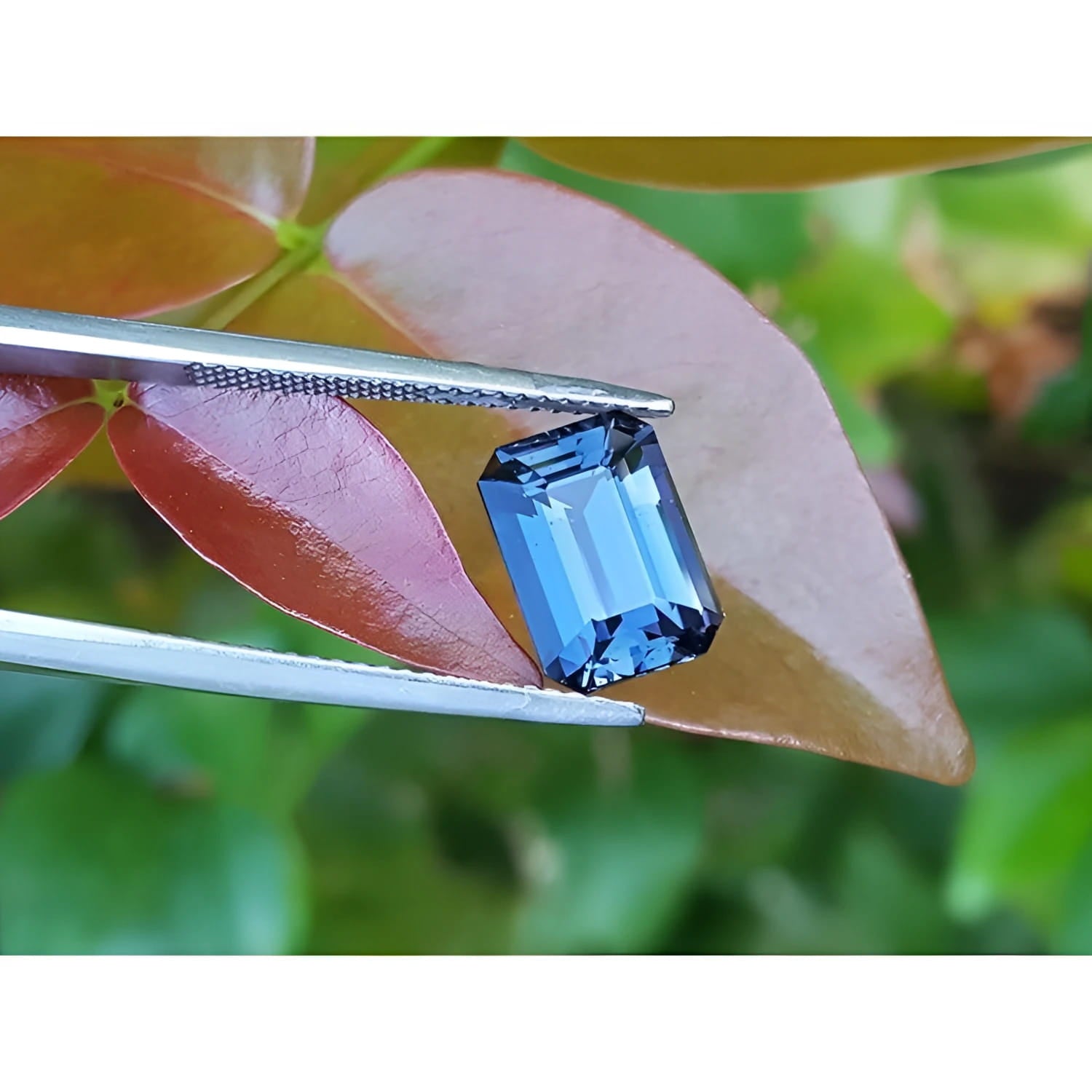3.90 ct untreated GIA certified blue changing to purple emerald-cut sapphire held by tweezers.
