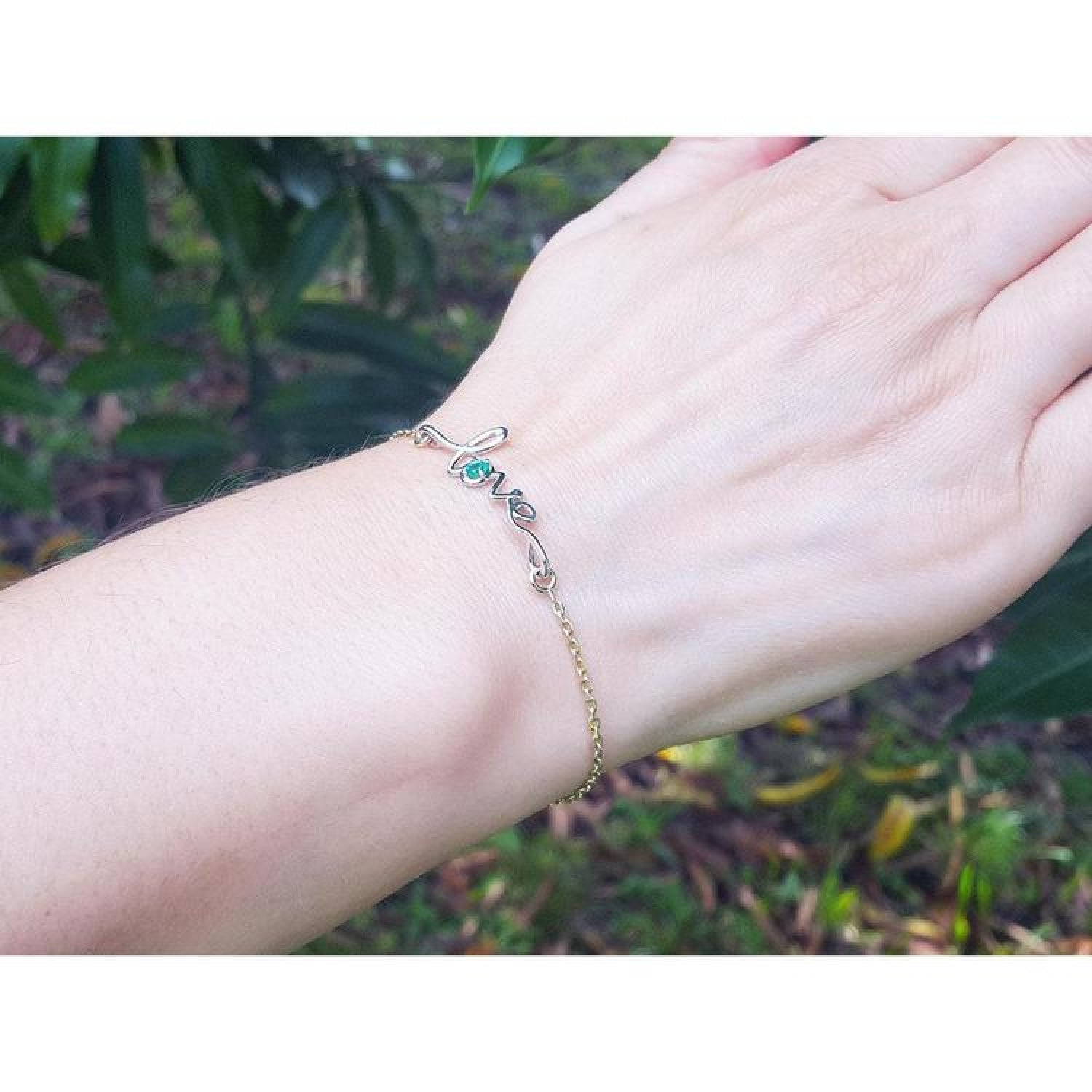 Emerald Love Bracelet in 14K yellow and white gold with a round cut emerald, worn on a wrist.