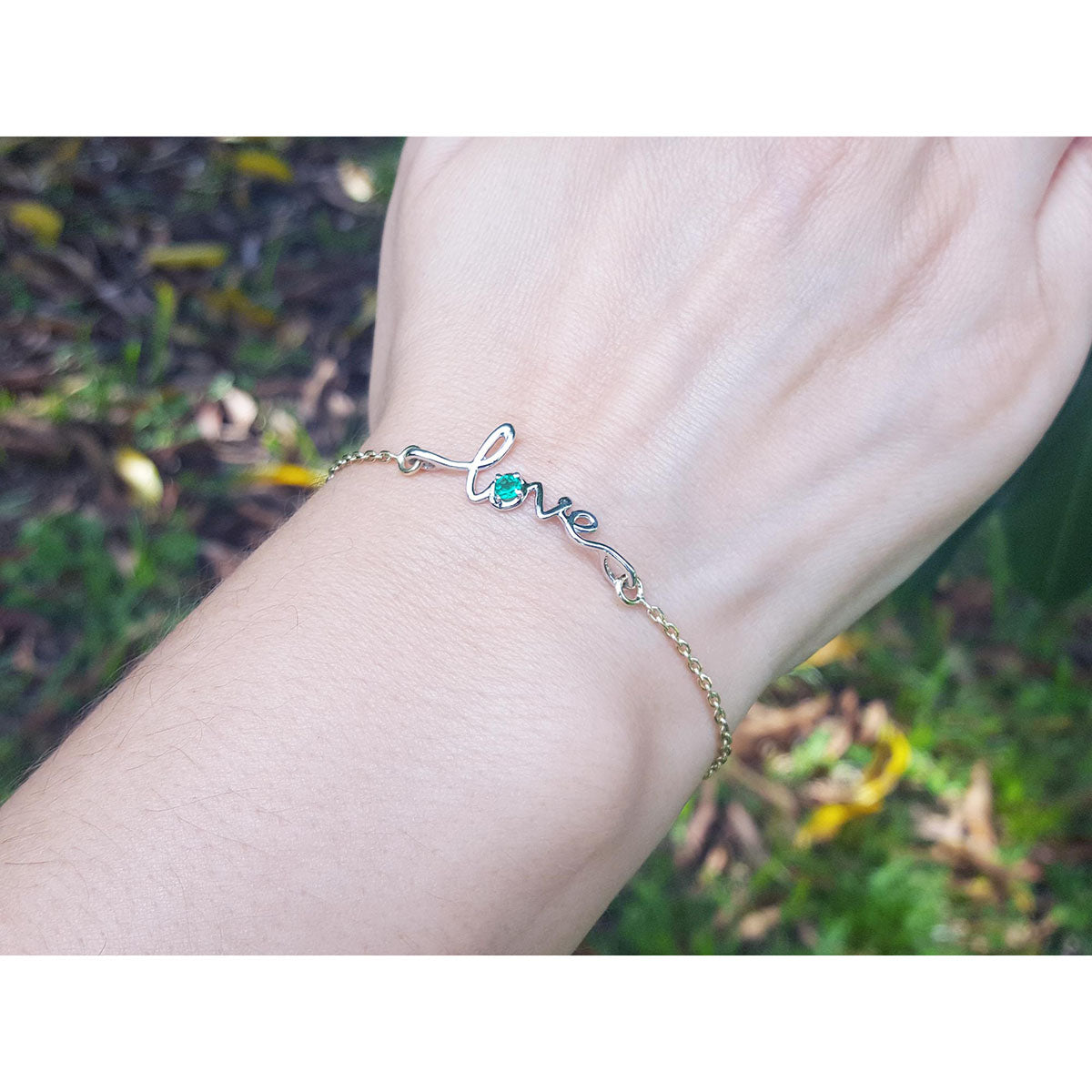 White and yellow gold bracelet with a natural emerald on a wrist against a natural background.