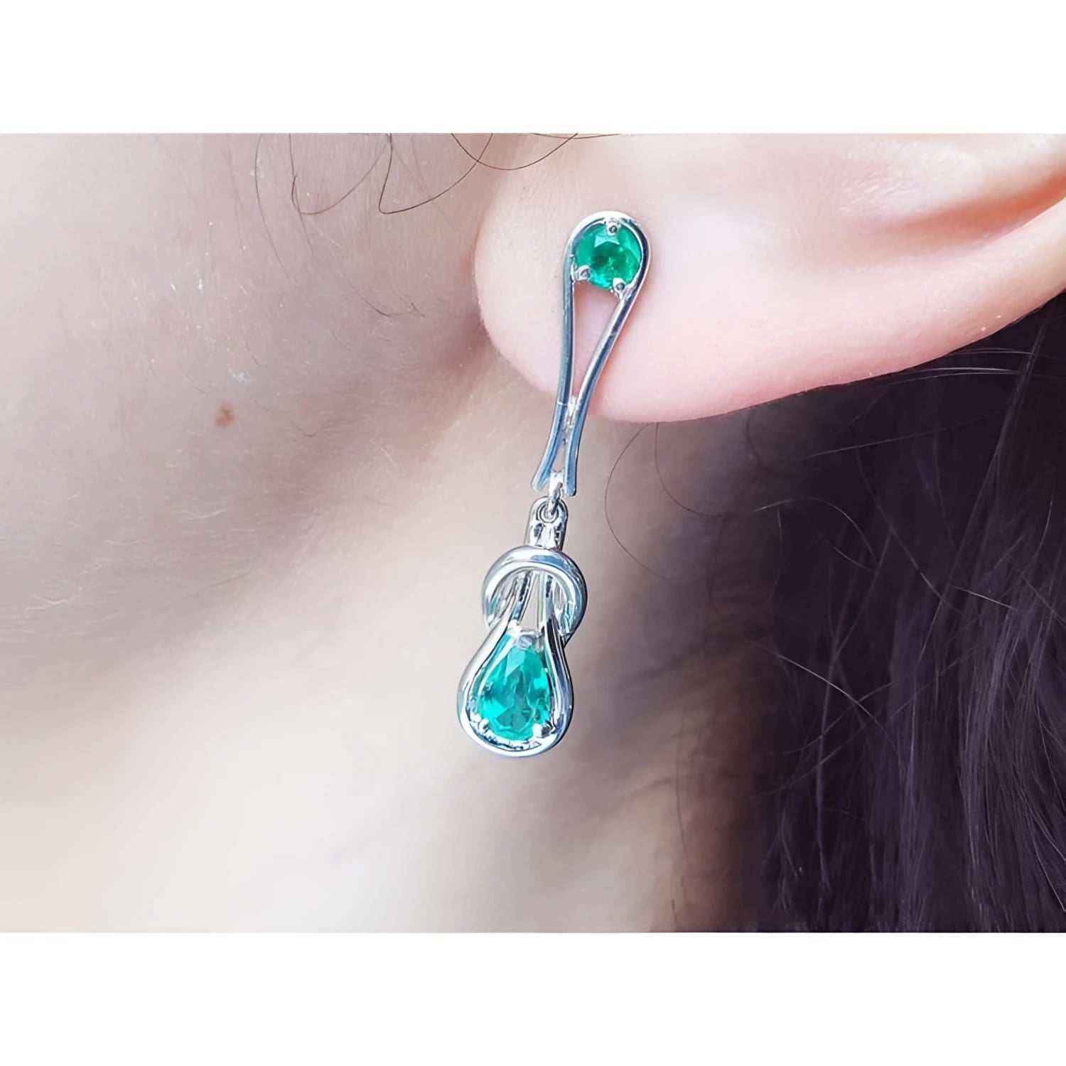 Love knot emerald earrings with pear-shaped Colombian emeralds in 14K white gold on an ear.