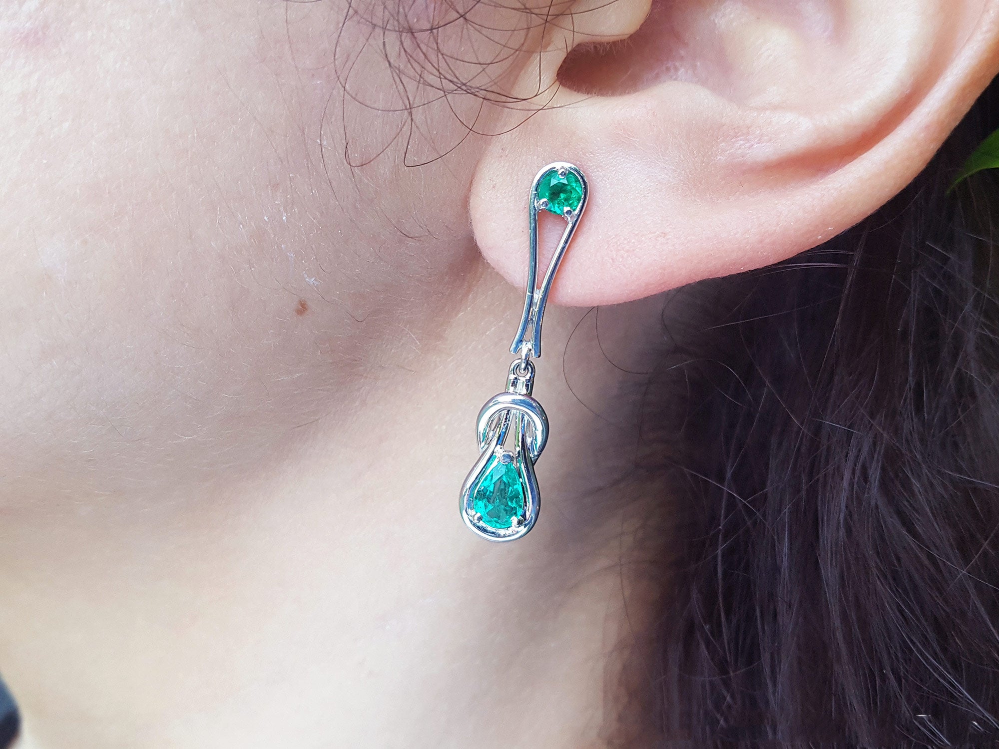 White gold Love Knot emerald earring worn by a person