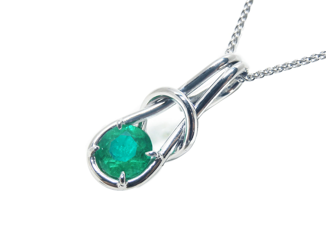 This love knot pendant necklace in white gold with a natural colombian emeralds displays its top and left- side profile. 