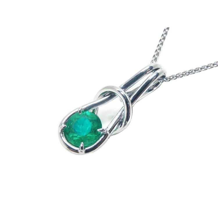 This love knot pendant necklace in white gold with a natural colombian emeralds displays its top and left- side profile. 