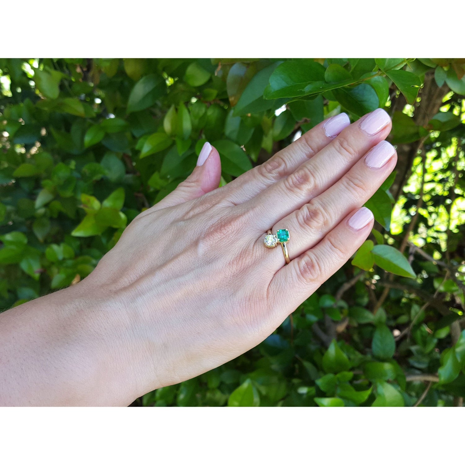 Hand wearing a two stone emerald and diamond ring in yellow gold.