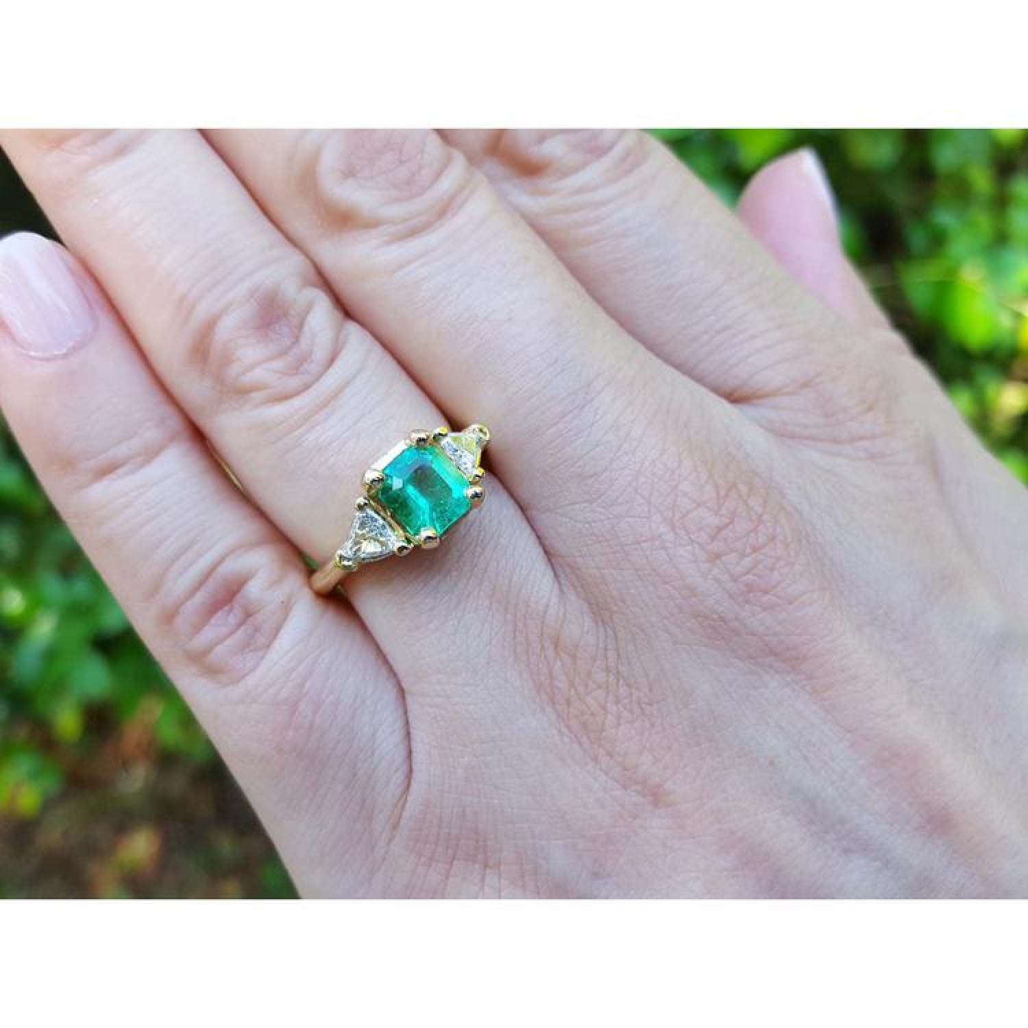 18K yellow gold three-stone ring with a vibrant Colombian emerald and two trillion-cut diamonds on a hand.