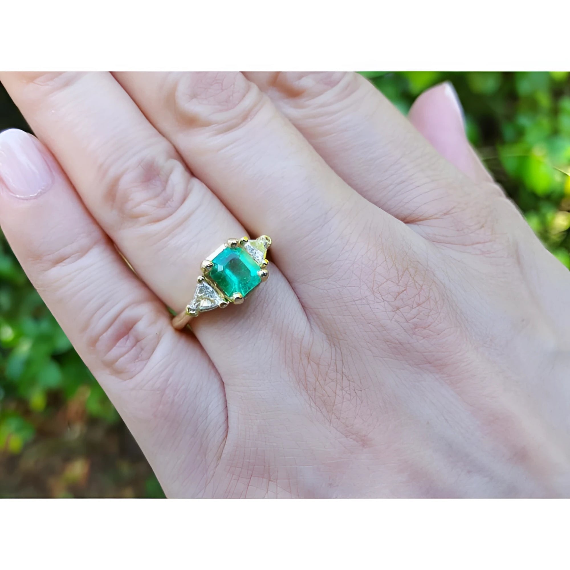 18K yellow gold three-stone ring with a vibrant Colombian emerald and two trillion-cut diamonds on a hand.