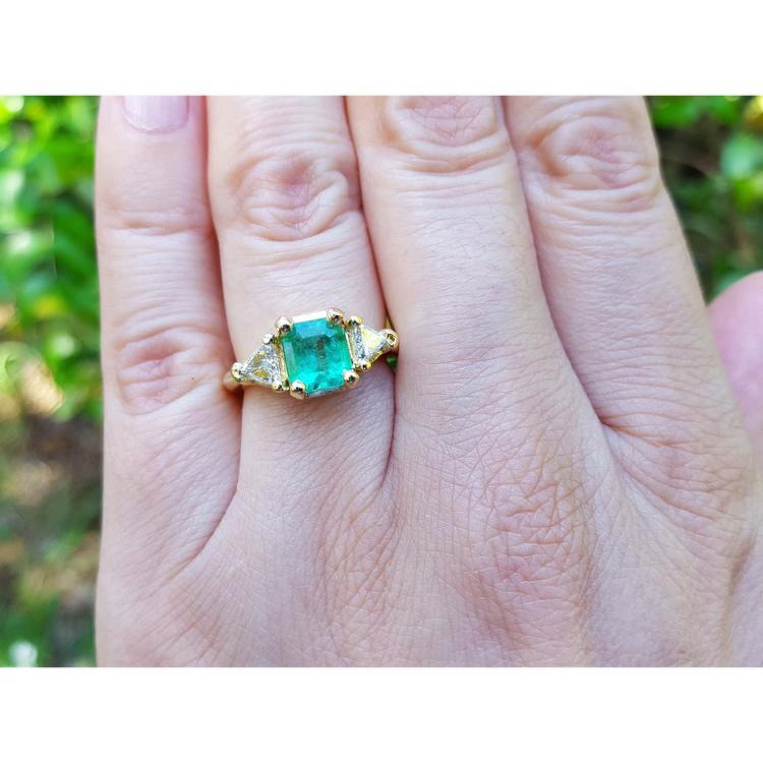 1.27 ct natural Colombian emerald three-stone ring in 18K yellow gold with two trillion-cut diamonds.