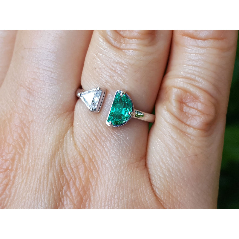 A close-up of a hand wearing a toi et moi emerald and diamond ring in white gold.