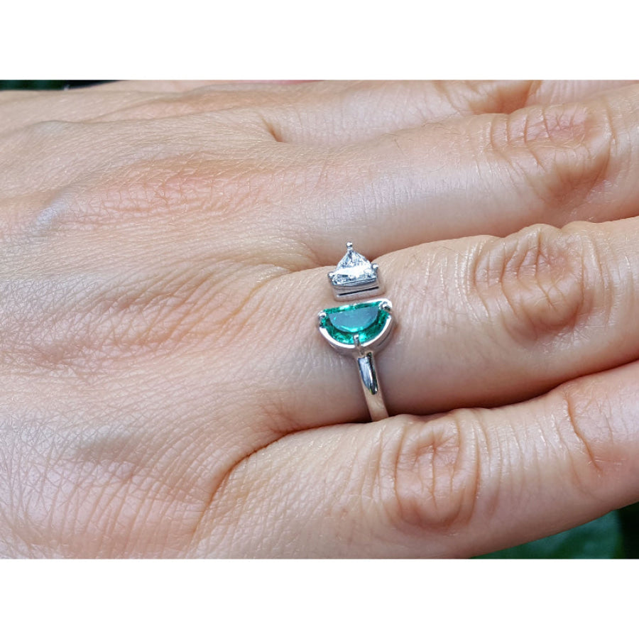 A negative space Toi et Moi ring features a half-moon-shaped natural Colombian emerald and a trillion-cut diamond, on a person's finger.