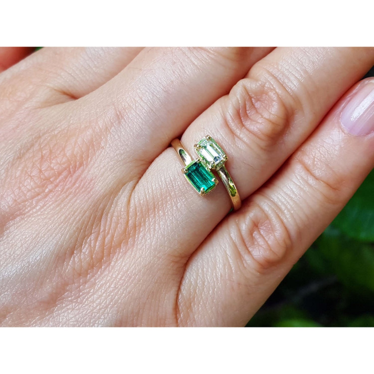 A close-up of a hand wearing two gold rings, one with a rectangular green emerald-cut gemstone and the other with a smaller round green stone.