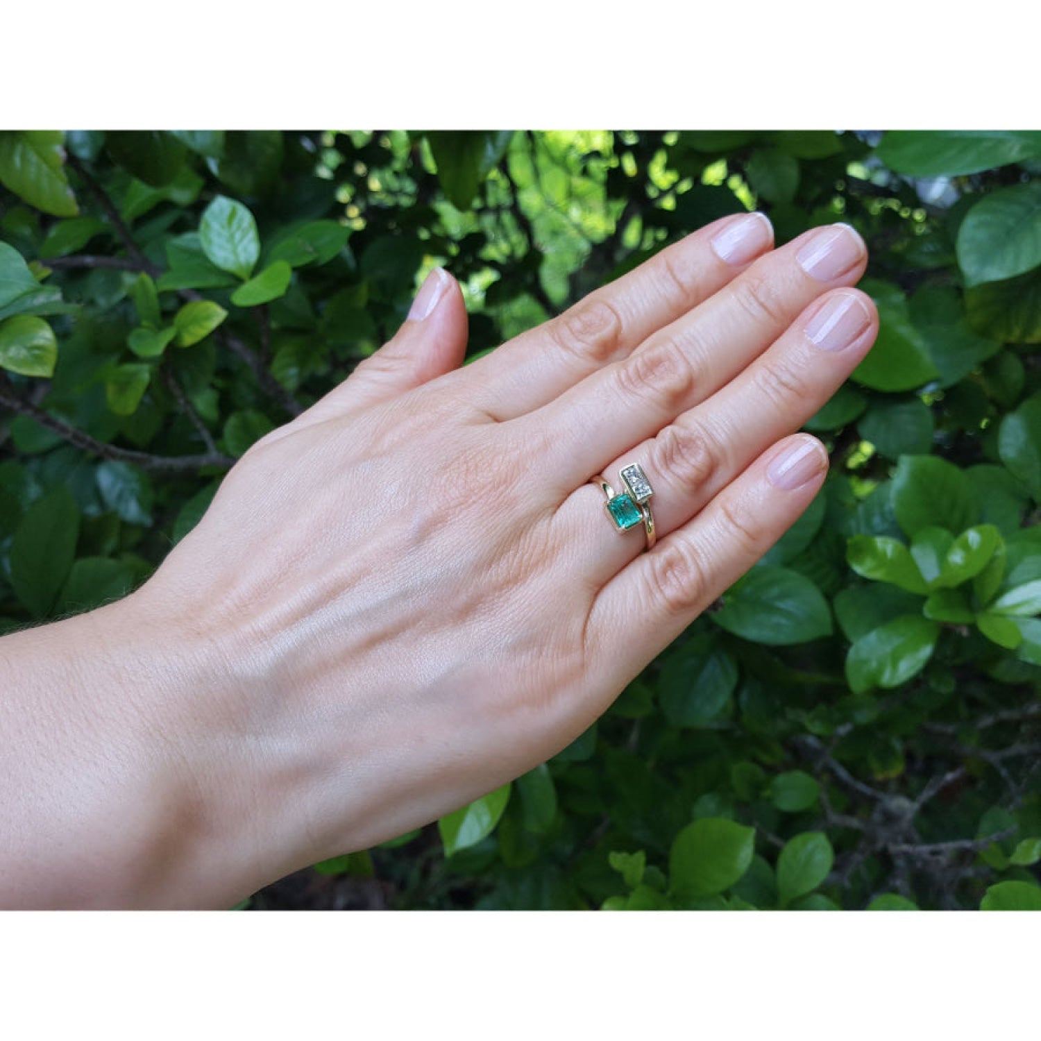 A you and me 18k yellow gold you and me ring worn on a person's ring finger against a background of green foliage.