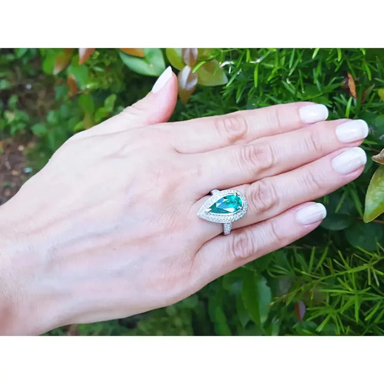 Una mano de mujer vistiendo un anillo de esmeralda colombiana corte pera con diamantes en oro blanco.
